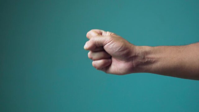 Close up of a male hand performing the scissors gesture from the rock paper scissors game against a solid blue studio backdrop.