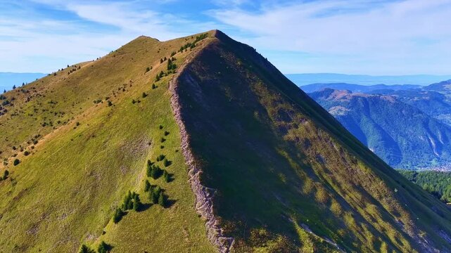 Drone 4K aerial view flying along a sharp alpine mountain ridge with green slopes and dramatic landscape under clear blue sky, cinematic forward motion in nature