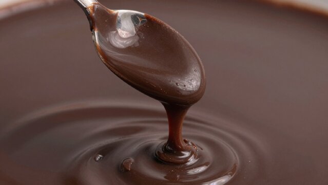 Close-up melted chocolate poured silver spoon bowl rich dark brown color appears thick smooth glossy texture h