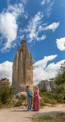 A happy lesbian couple holding hands in front of the imposing sandstone formations of Orgues d'Ille-sur-Têt under a blue sky in France.
