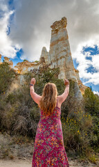 Rear view of a woman in a floral dress, with her arms raised like a priestess, admiring and venerating the towering fairy chimneys and sand columns of Orgues d'Ille sur Têt in France.