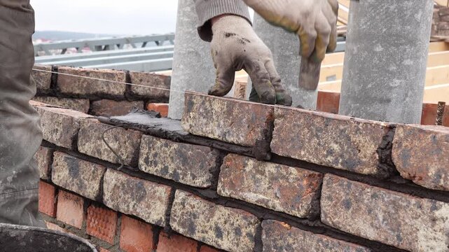 Professional bricklayer building a brick wall at the construction site using a trowel and mortar