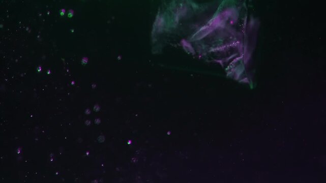 Ice cube falling into water with oxygen bubbles, frost patterns, and purple green light reflections. Concepts for beauty advertising, menu designs for bars and restaurants, cryotherapy.