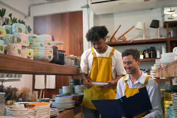Fototapeta premium Two men in yellow aprons organizing shelves filled with colorful ceramic dishes
