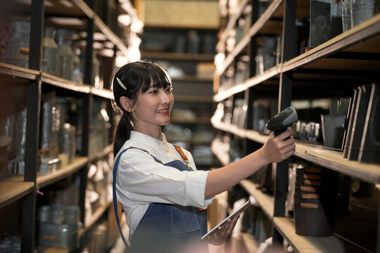 Young woman in warehouse scanning inventory with barcode reader and tablet