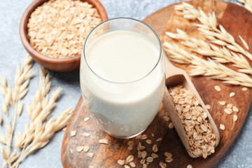 Oat milk in glass and flakes on grey textured table, closeup
