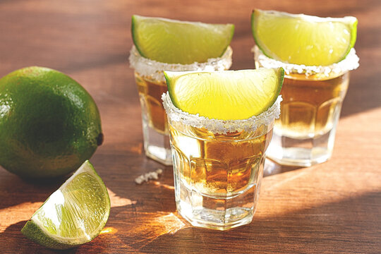 Slices of fresh lime on tequila glasses placed on a wooden table, in daylight, no people