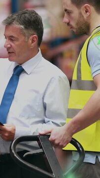Vertical video: Manager pointing clipboard while worker gripping jack in warehouse, preparing stock