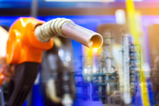 Fuel Nozzle and Refinery Industry, An orange fuel pump nozzle is shown in a double exposure with a glowing industrial oil refinery, representing petroleum and gas production.