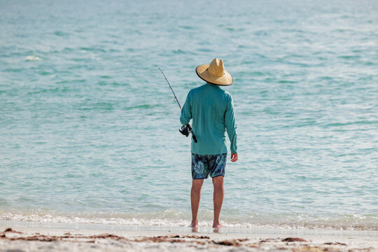 Saltwater fisherman fishing from the beach. Man surf cast fishing from the shoreline of the Gulf of America, Florida.