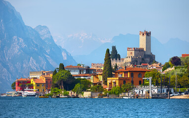 Ancient tower and fortress in old town Malcesine at Garda Lake, Veneto region, Italy. High snowbound top mountains on background. Summer landscape with colorful houses and green trees.