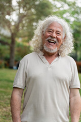 Funny senior man with long curly hair laughing in park. Happy retirement
