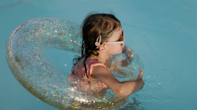 Cute funny toddler girl relaxing on inflatable toy ring floating in pool have fun during summer vacation. Child having fun in swimming pool. 