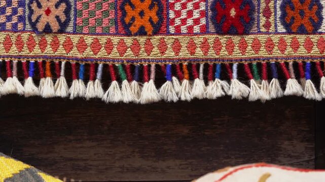 Close-up of a colorful traditional Anatolian kilim rug with intricate geometric patterns and white tassels, showcasing authentic textile craftsmanship against a rustic dark wooden background. 