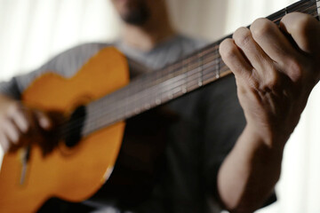 Fototapeta premium Close-up of Musician Hands Playing Acoustic Guitar. Detailed view of fingers strumming strings on a wooden acoustic guitar. Focus on the soundhole and strings with a blurred background