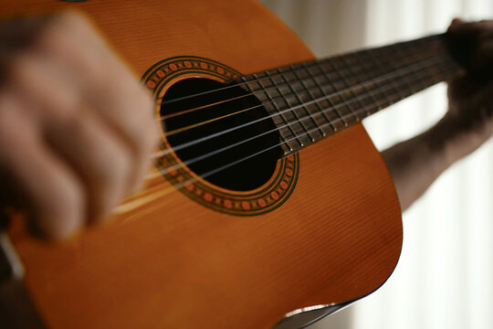 Close-up of Musician Hands Playing Acoustic Guitar. Detailed view of fingers strumming strings on a wooden acoustic guitar. Focus on the soundhole and strings with a blurred background