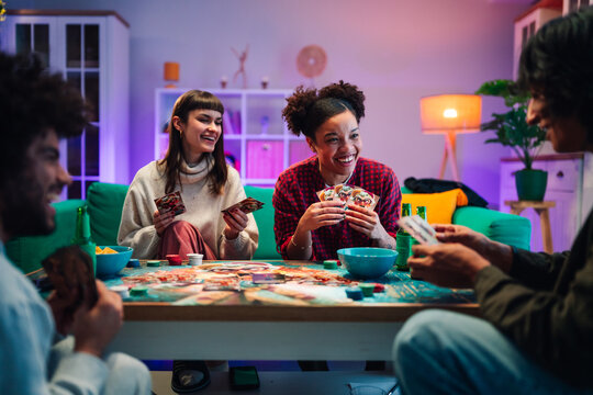 Diverse friends laughing while playing cards and board games together during a fun social gathering at home