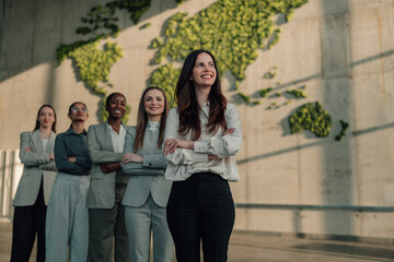 Fototapeta premium Group of diverse businesswomen standing with arms crossed, showing unity and leadership against a world map made of plants