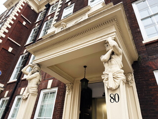 Fototapeta premium Historic London, UK building entrance with classical atlantes statues flanking decorative doorway number 80
