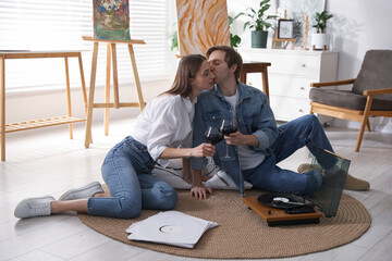 Fototapeta premium Romantic date. Couple with glasses of wine listening to vinyl record on floor indoors