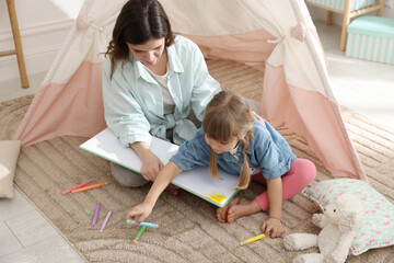 Mother and her daughter drawing in sketchbook together near toy wigwam at home © New Africa