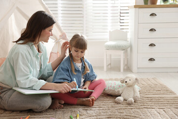 Mother and her daughter drawing in sketchbook together near toy wigwam at home, space for text © New Africa