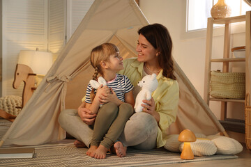 Mother and her daughter with toys near wigwam at home © New Africa