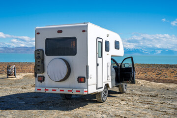White off-road truck camper parked by a turquoise lake with mountain views under a blue sky, adventure travel and overlanding concept