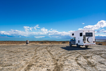 White camper truck parked on a dirt plateau overlooking a turquoise lake and mountain range in Patagonia, Argentina