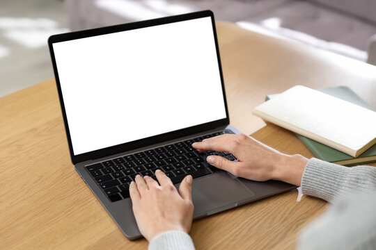 Woman typing on laptop at wooden table indoors, closeup