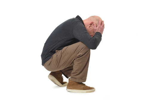 side view of a stressed man squatting looking down hands on face