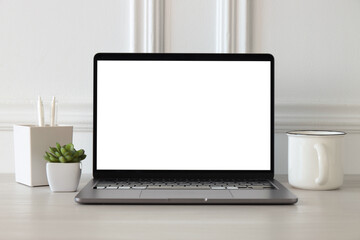 Fototapeta premium Stylish workplace. Laptop with blank screen, cup of drink, houseplant and decor on white wooden table