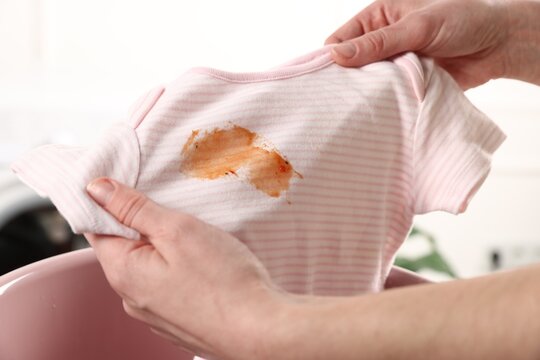 Woman washing stained kid's shirt in basinet indoors, closeup