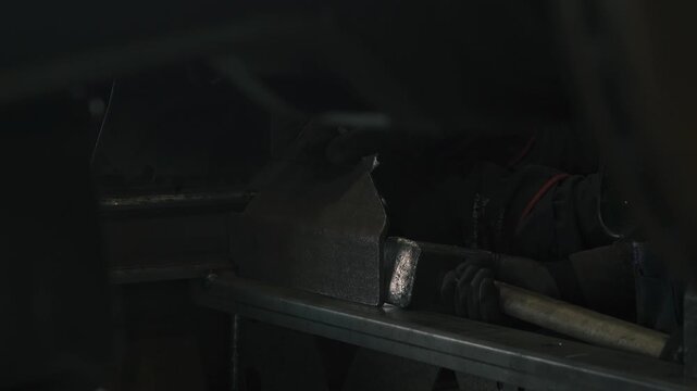 In a busy workshop, a skilled worker expertly hammers a metal part before welding it to an agricultural semi-trailer, demonstrating exceptional craftsmanship and precision.