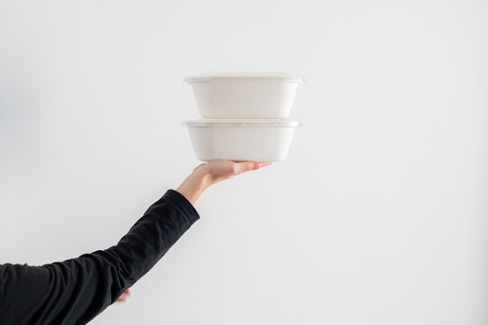 Una mujer sostiene dos envases de comida para llevar de cart&oacute;n reciclado, aislados sobre fondo blanco. Concepto de packaging alimentario, delivery y consumo responsable.