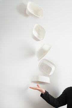 Varios envases de comida para llevar de cart&oacute;n, flotando en el aire. Una mujer lanza envases de delivery. Concepto de packaging alimentario y consumo responsable. Fotomontaje.
