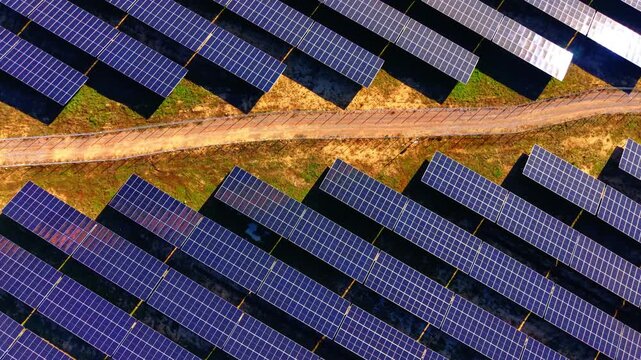 Solar module arrays separated by a dirt maintenance path on grassy terrain. High angle aerial view of solar panels with service road.