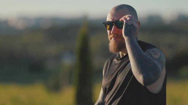 Tattooed biker man removing sunglasses outdoors