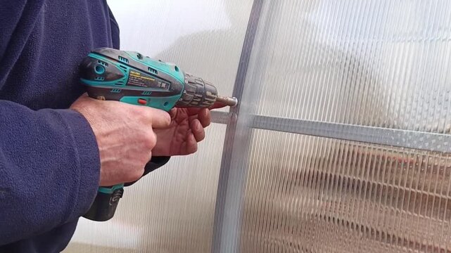 The process of fastening polycarbonate when installing a greenhouse using a screwdriver. Hands while working with a screwdrive.