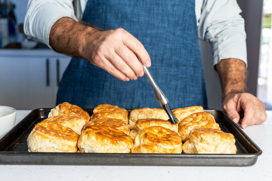 Butter being brushed on freshly baked biscuits on a baking sheet  