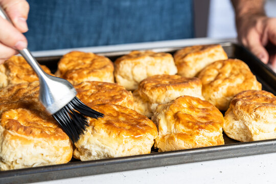 Butter being brushed on freshly baked biscuits on a baking sheet  