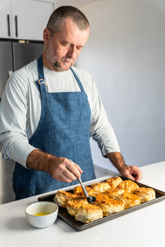 Man brushing butter on fresh biscuits in a kitchen 