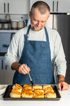 Man brushing butter on fresh biscuits in a kitchen 