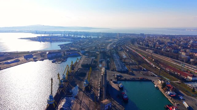 Panoramic aerial view the intersection of a maritime terminal, extensive railway tracks, and the city residential border. Integrated transport hub with railway station and sea port.