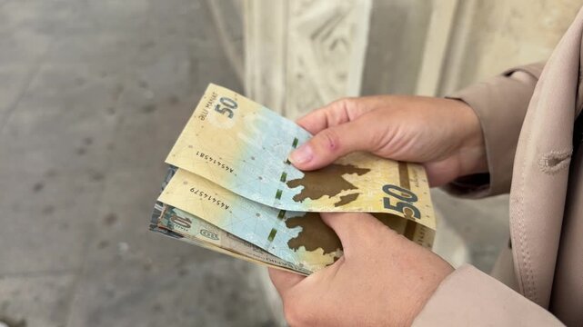 Hands holding Azerbaijani manat banknotes, conveying personal finance, budgeting, spending power, everyday transactions, practical money awareness, and consumer planning.