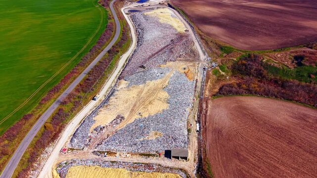 Designated landfill section filled with trash, bordered by a road and agricultural land. Aerial perspective of waste disposal cell and birds flying over garbage.