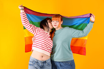 Lovely lesbian couple with rainbow flag on yellow background. LGBT concept