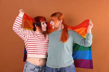 Lovely lesbian couple with rainbow flag on brown background. LGBT concept