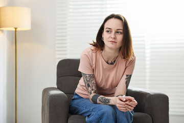 Obraz premium Beautiful woman with stylish tattoos and piercings on armchair at home. Space for text