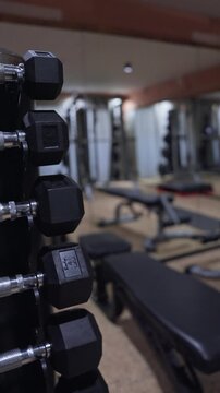 Close up vertical shots track down hex dumbbells with knurled chrome handles in an upscale Alpine hotel gym as focus shifts and pulls back, benches and mirrors blur.